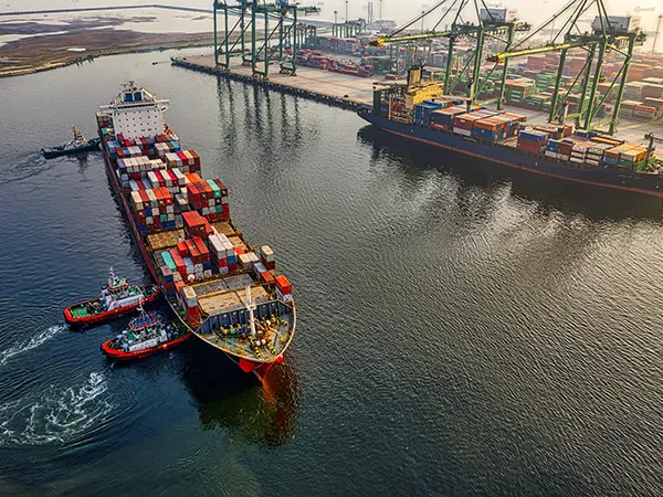 Aerial view of a busy cargo port with cranes and tugboats maneuvering container ships, highlighting global trade infrastructure and logistics ope